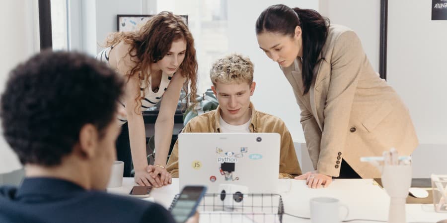 Team of young professionals collaborating around a laptop in a modern office setting, symbolizing teamwork, project planning, and workplace collaboration.