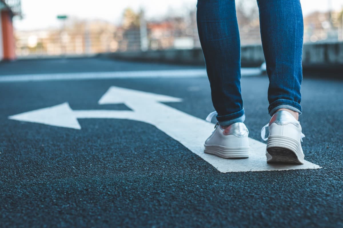 Close up of a person's shows walking in direction of road arrows